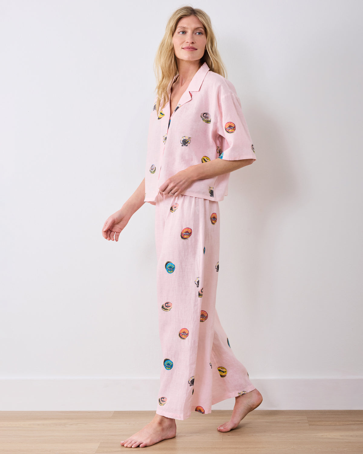 Side view of a model wearing a pink cropped short-sleeve top and wide-leg pants with embroidered caviar tin and shell motifs.