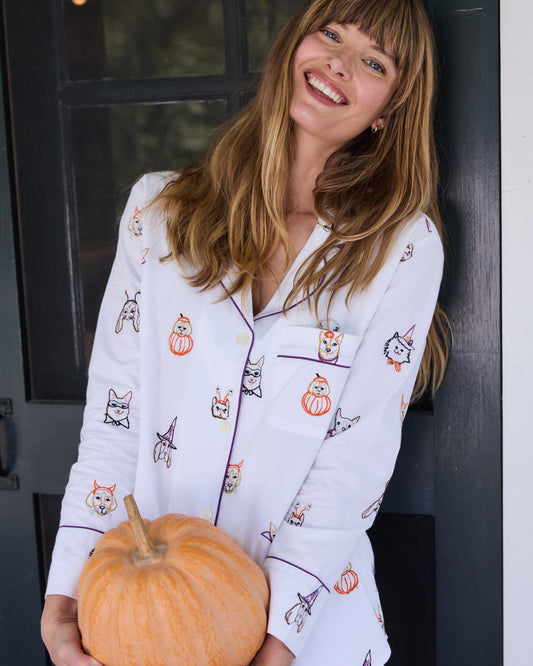 Close view of a person wearing a white dog-print pajama top with purple piping and holding a pumpkin.