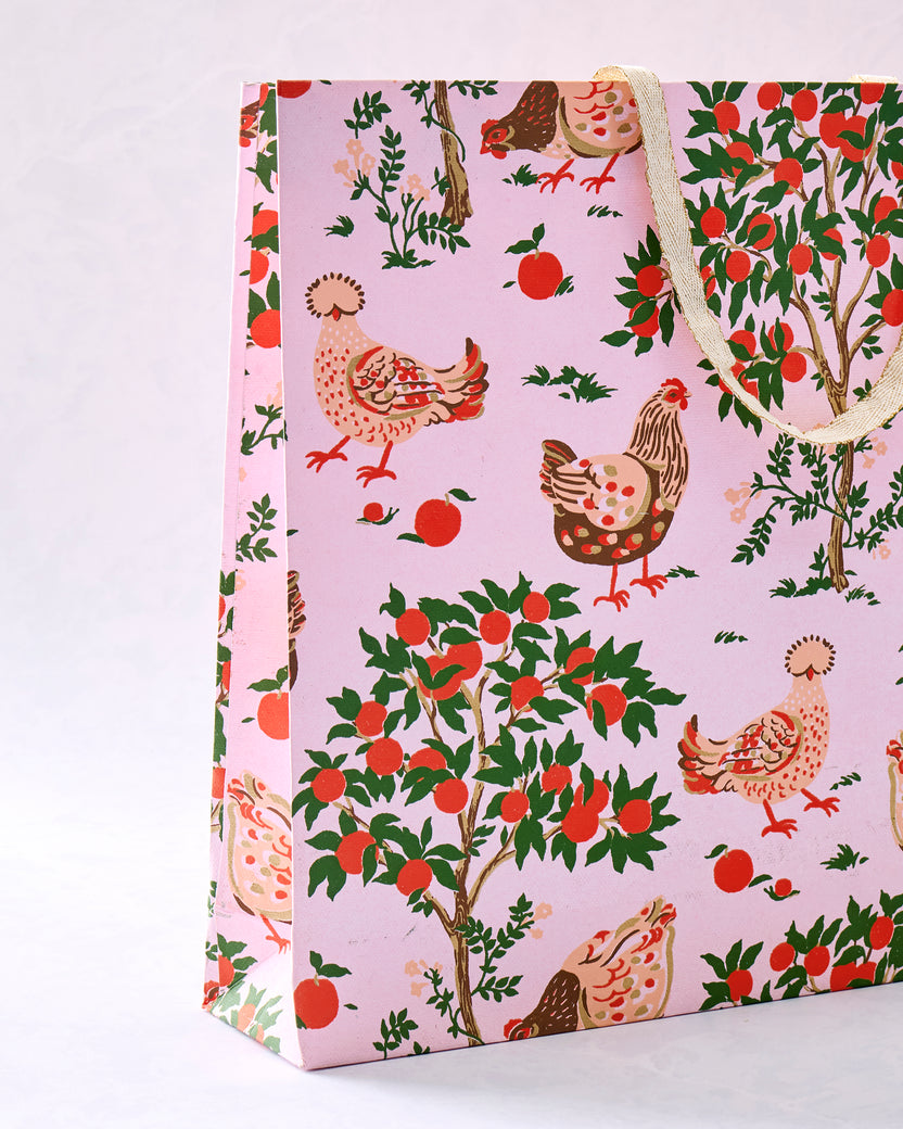 Pink Hen House gift bag with chicken and apple print and cream-colored handles.