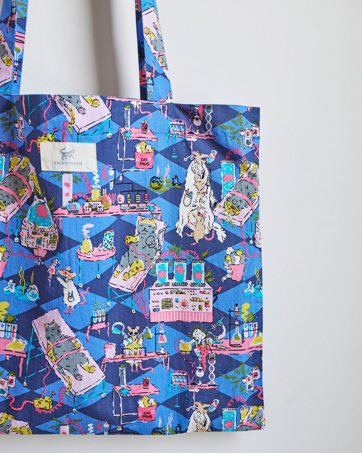 Close view of a blue tote bag printed with colorful laboratory scenes featuring cats, mice, and scientific equipment.