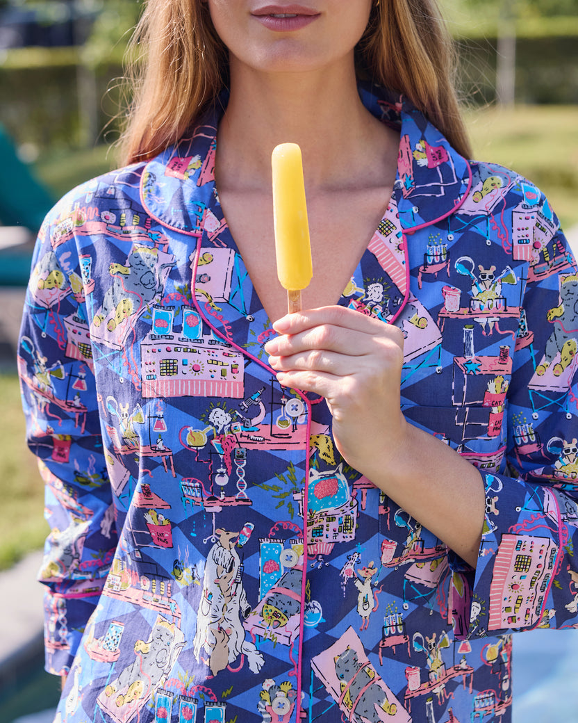 Close view of a blue button-down sleep shirt with a colorful mice-and-laboratory print, while a person holds a yellow popsicle.