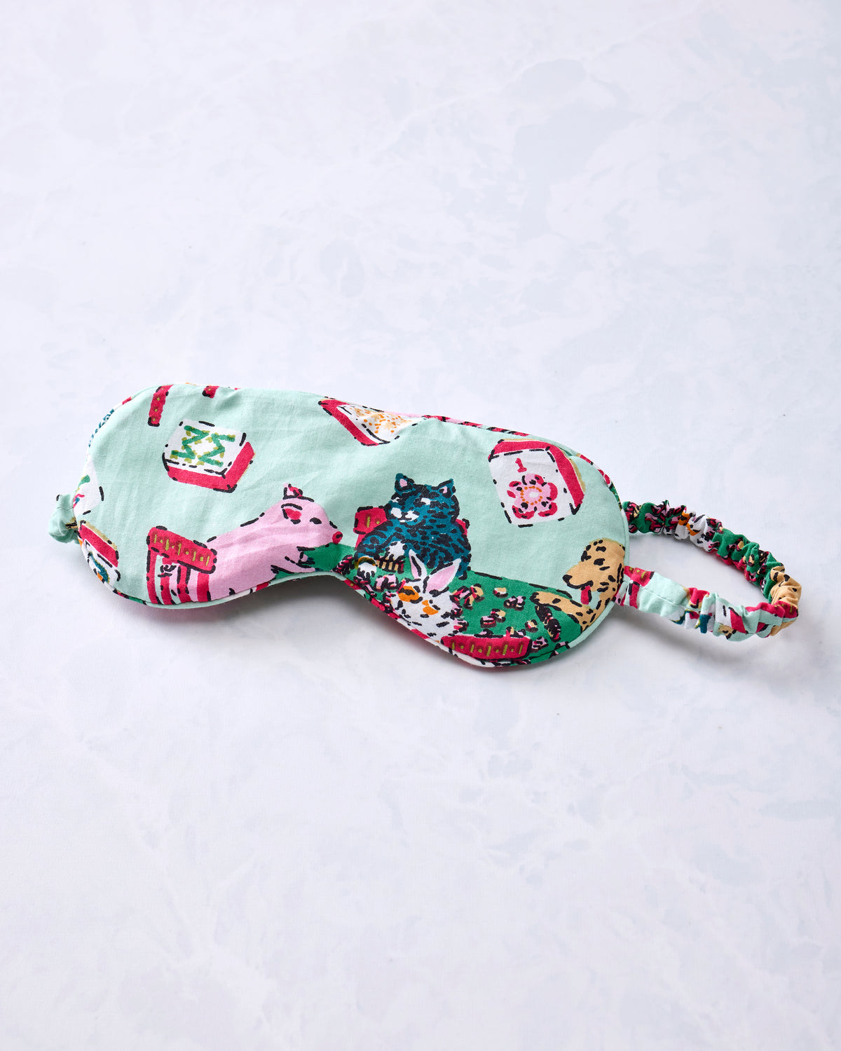 Pale jade eye mask with an adjustable printed strap and Mah Jongg-themed animal and game-table print.
