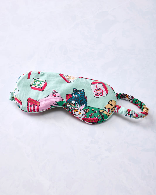 Pale jade eye mask with an adjustable printed strap and Mah Jongg-themed animal and game-table print.