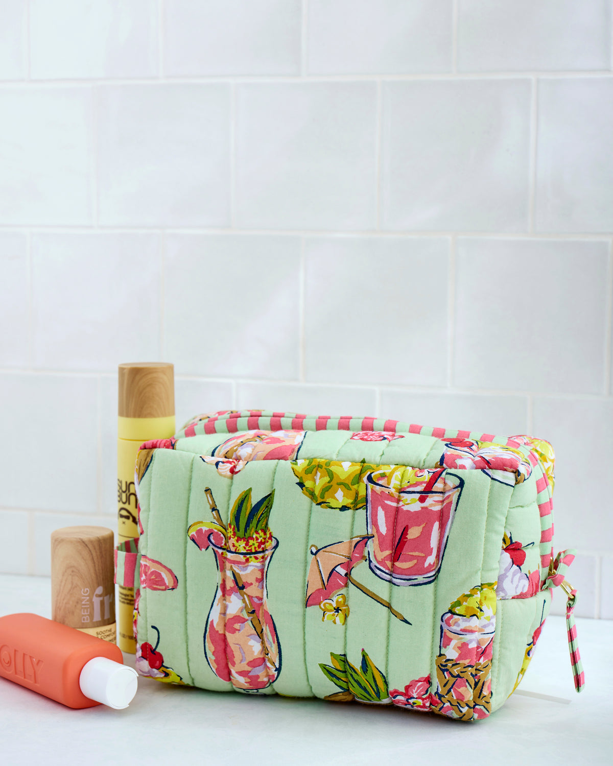 Quilted Paradise Punch pouch with a light green background and colorful tropical drink illustrations, shown with toiletry bottles.