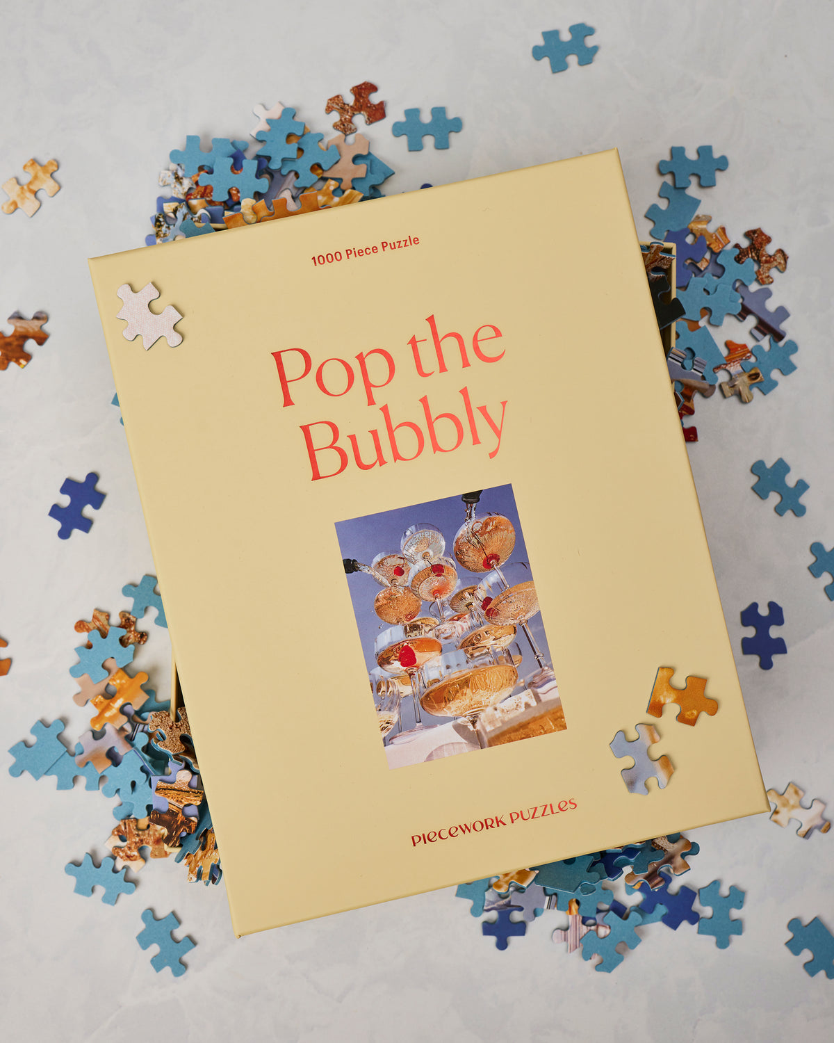Pop the Bubbly 1000-piece puzzle box surrounded by loose blue, white, and multicolored puzzle pieces.