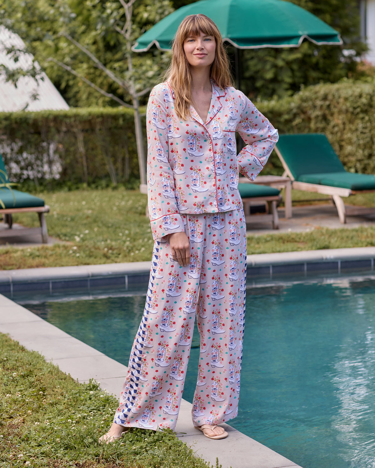 Full-length front view of the long-sleeve, wide-leg pajama set beside a swimming pool, showing the floral cowboy-boot print and side panel.