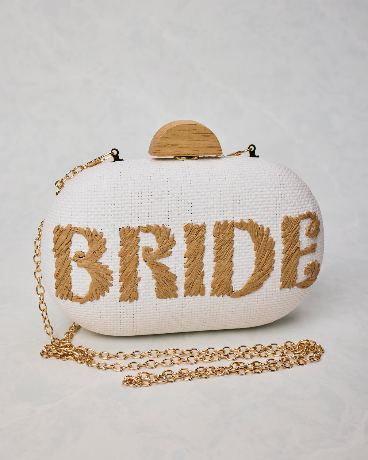 White Bride clutch with tan embroidered lettering, a wood-toned clasp, and a gold chain strap.