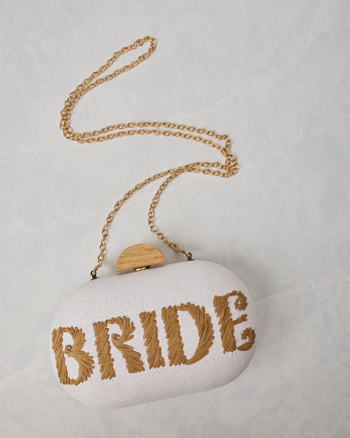 Angled view of the white Bride clutch with its gold chain strap and wood-toned clasp.