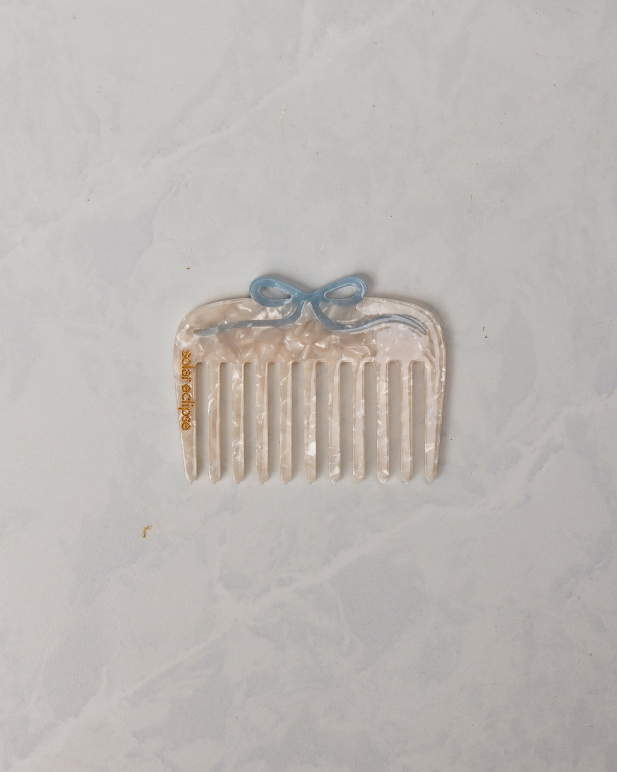 Translucent wide-tooth pocket comb with a blue bow-shaped detail and Solar Eclipse lettering.