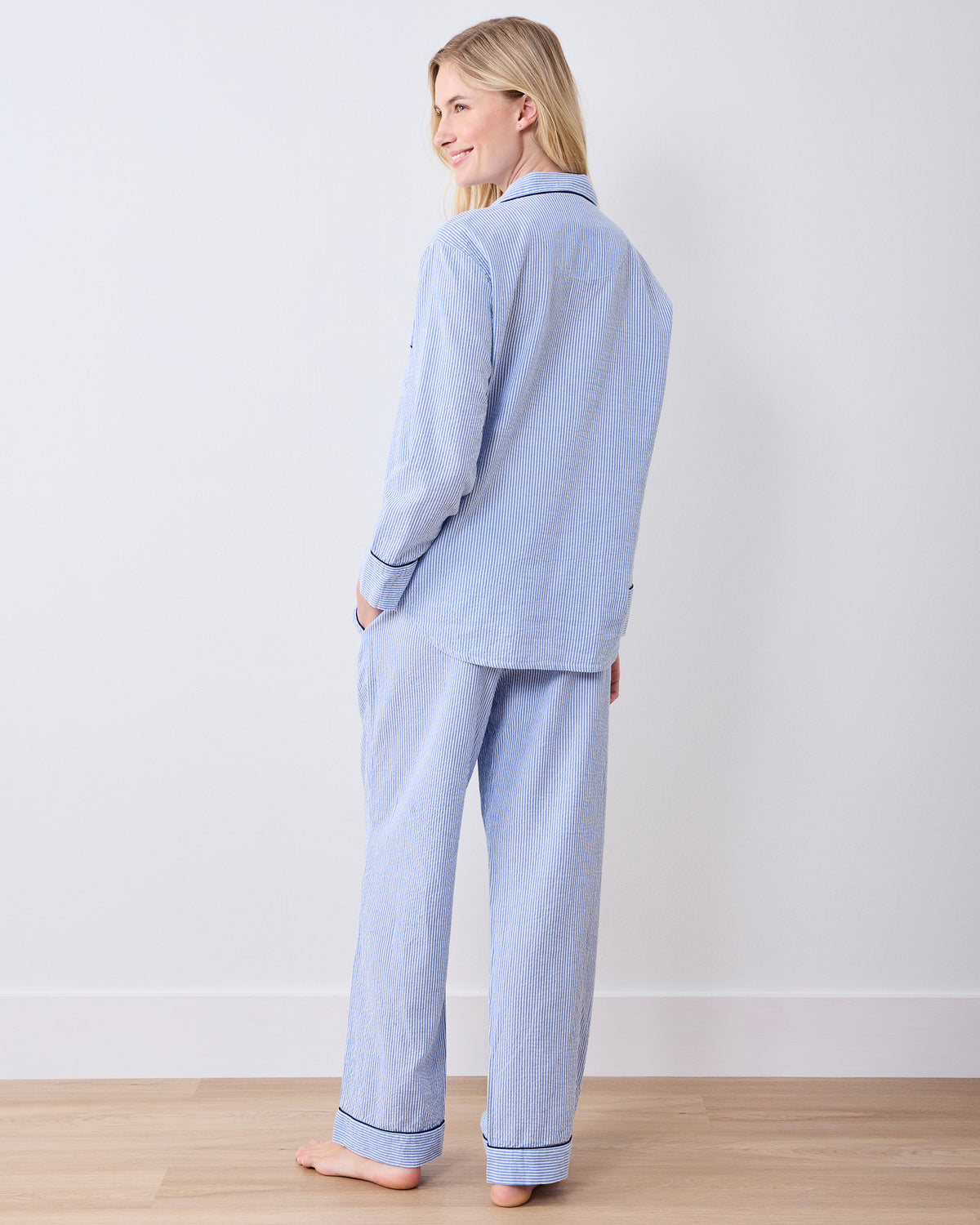 Rear three-quarter view of a blue-and-white striped long pajama set with dark piping at the cuffs