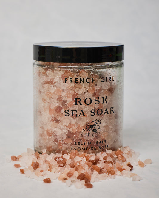 Close-up of a French Girl Rose Sea Soak jar with pink and white bath salts spilling onto the surface.