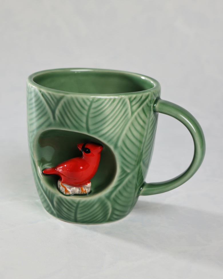 Green textured mug with a handle and a recessed alcove containing a red cardinal figure.