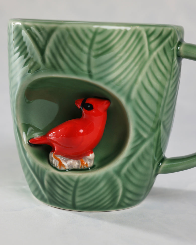 Green leaf-patterned mug with a red cardinal figure in a recessed front alcove and a handle on the right.