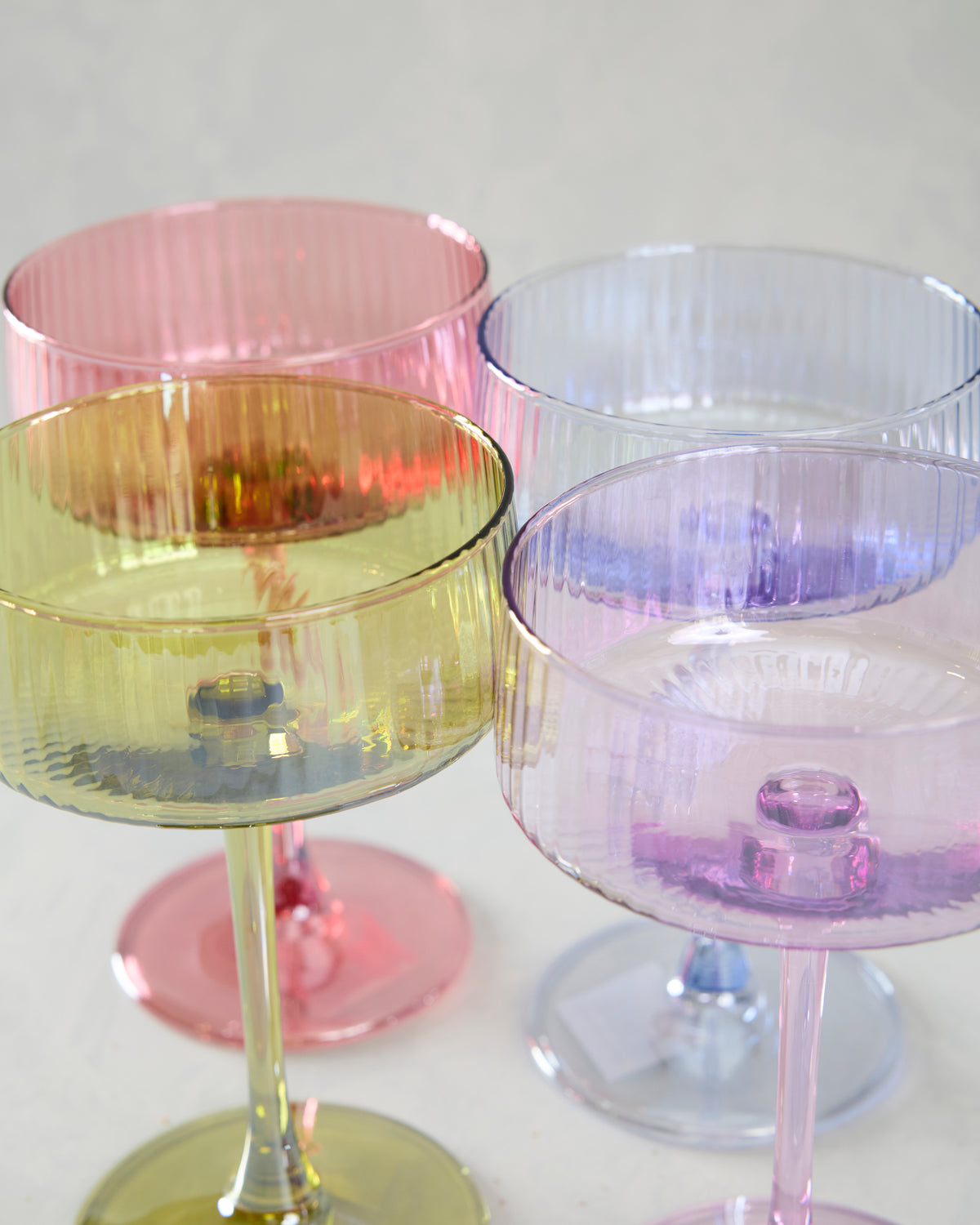 Close-up of four assorted translucent cocktail coupe bowls with vertical fluting and colored rims.