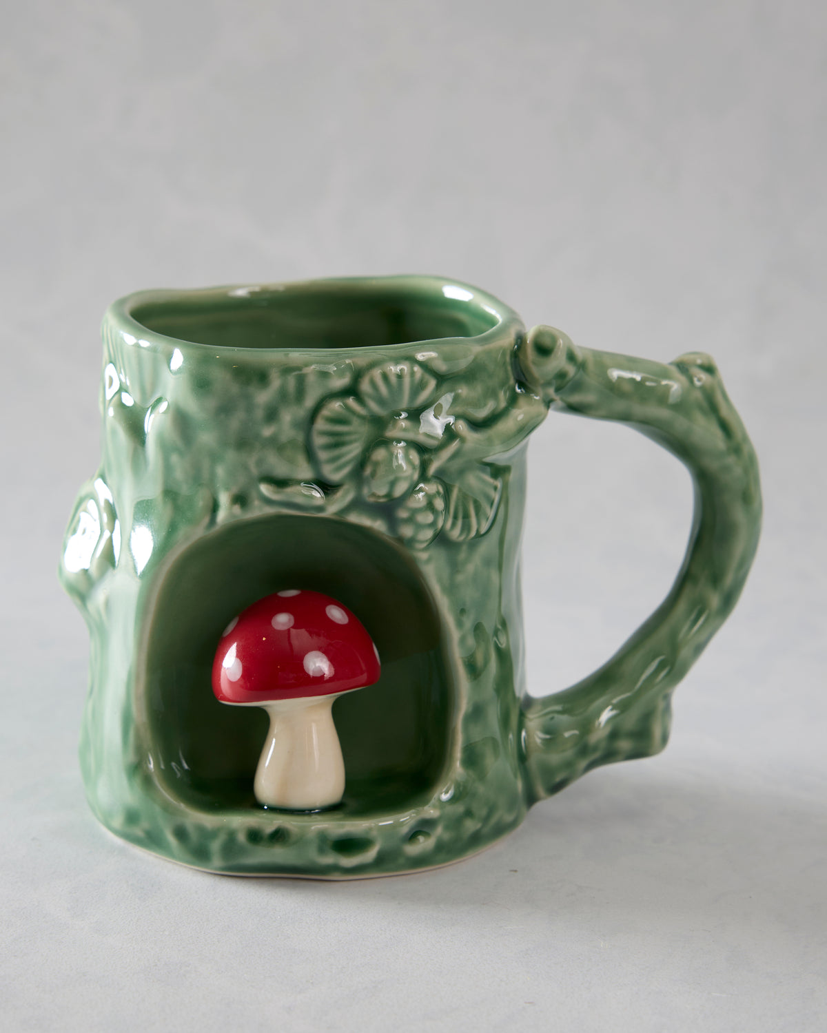 Green textured mug with a sculpted handle and a front alcove containing a red-and-white spotted mushroom.