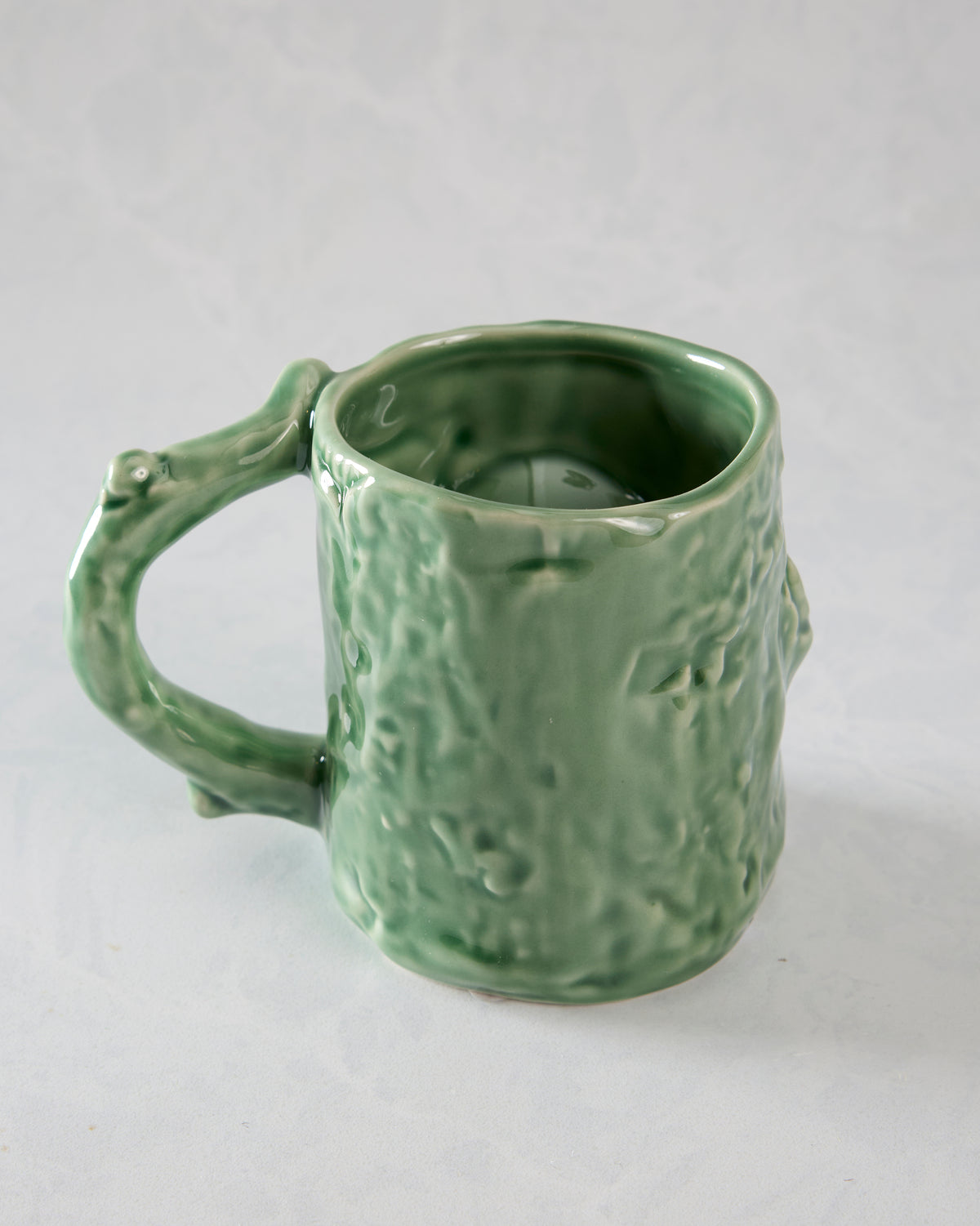 Rear three-quarter view of a green textured mug showing the open top, sculpted handle, and raised woodland-style details.