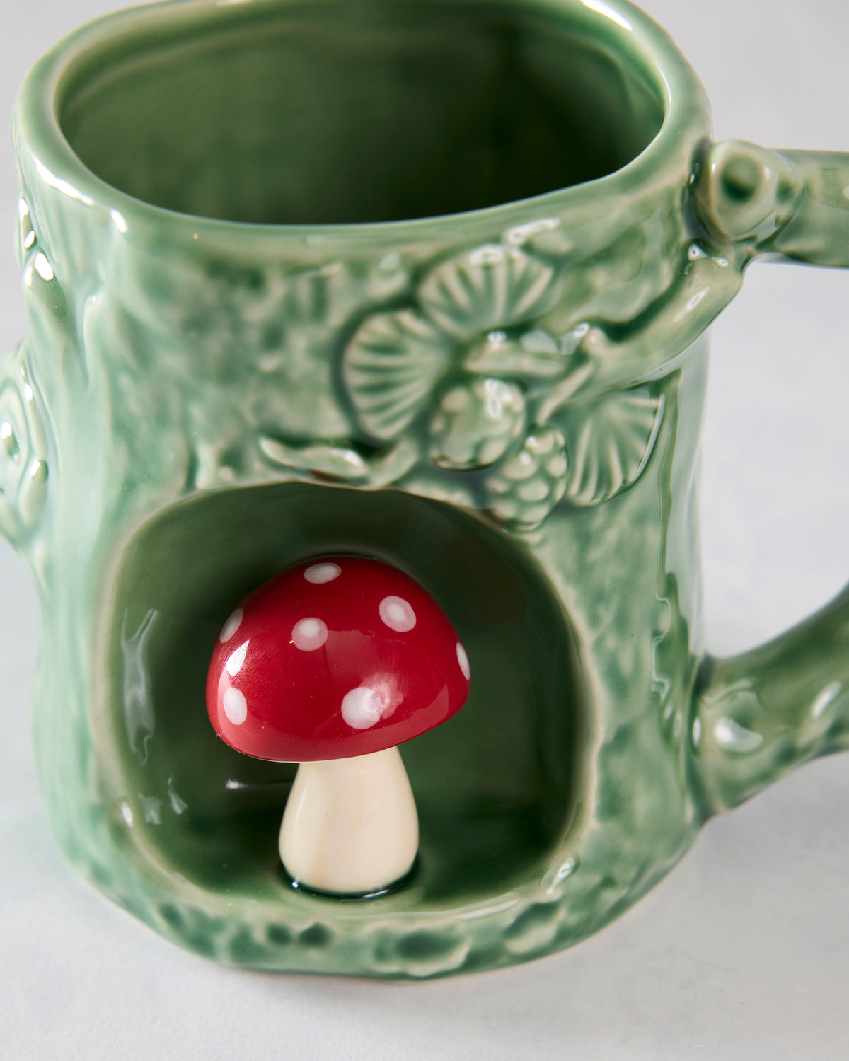 Close-up of the green textured mug’s front alcove with a red-and-white spotted mushroom and raised woodland details above it.