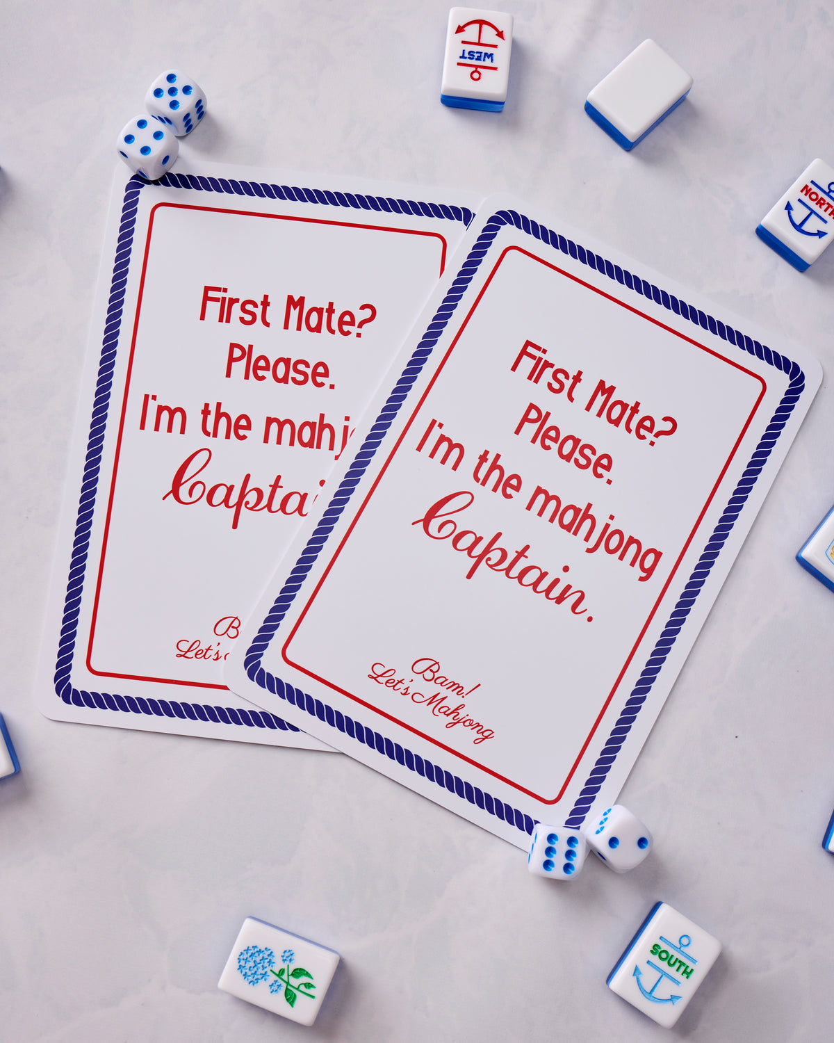 Two Nantucket mahjong cards overlapping on a tabletop, surrounded by nautical-patterned tiles and dice.