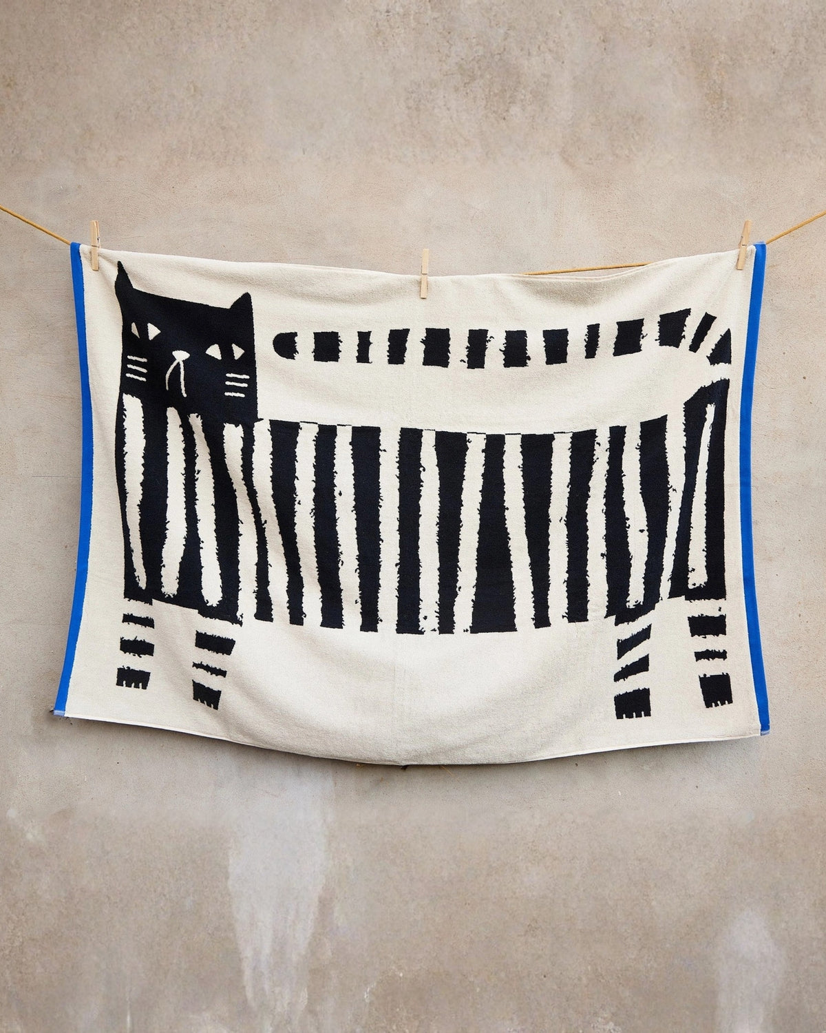 Lazy Cat XL sheet towel hanging from a clothesline, showing a black cat and piano-key pattern.