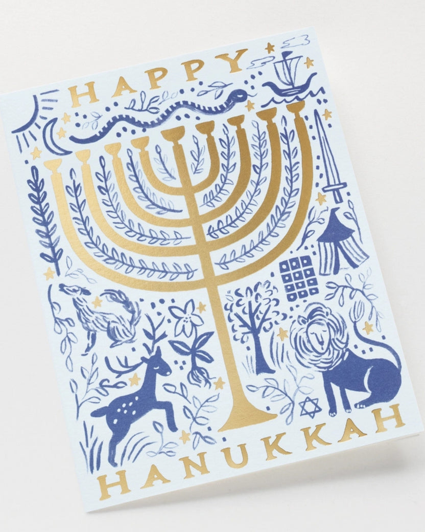 Close angled view of a Hanukkah greeting card with a blue and gold menorah design and the words “HAPPY HANUKKAH.”