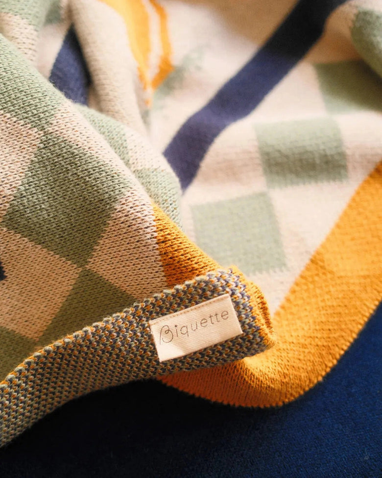 Close-up of the Un Beau Poisson throw showing its multicolored patterned edge and Biquette label.