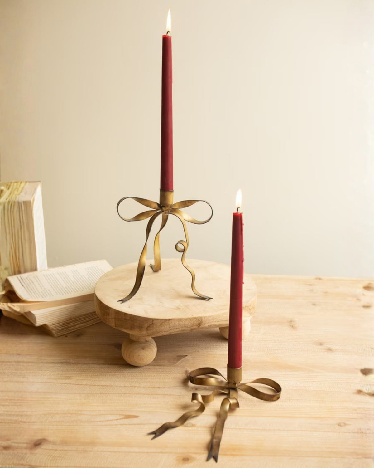 Two antique brass bow taper candle holders displayed with red lit taper candles on a wooden table