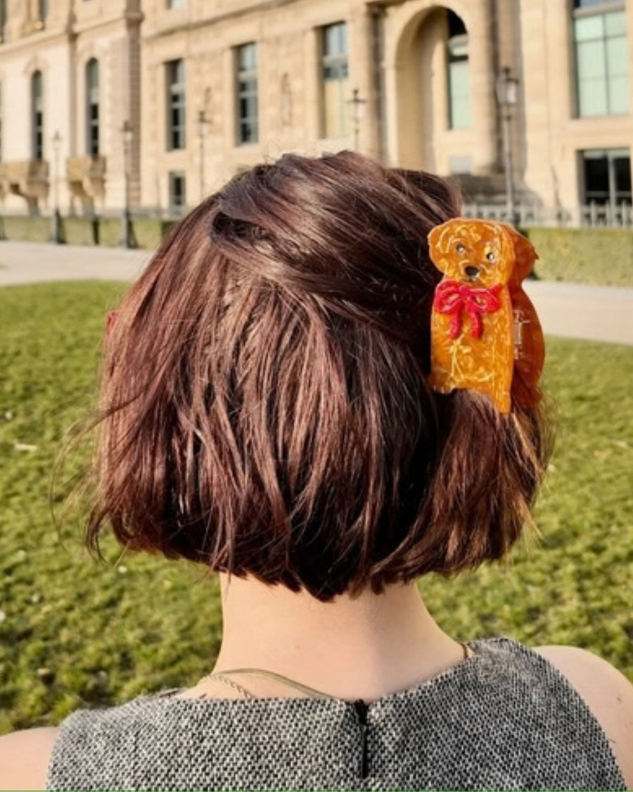 Brown puppy-shaped hair claw clip with a red bow, shown worn in short brown hair.