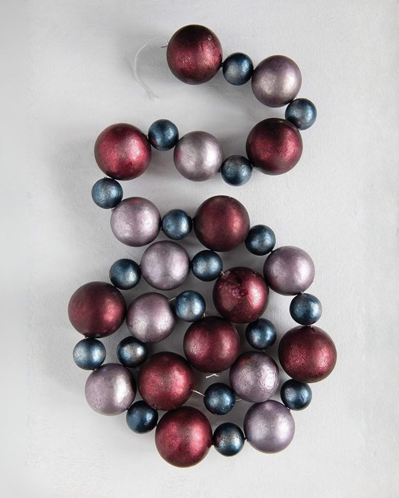 Christmas ball garland loosely coiled to show alternating burgundy, blue-gray, and mauve balls.