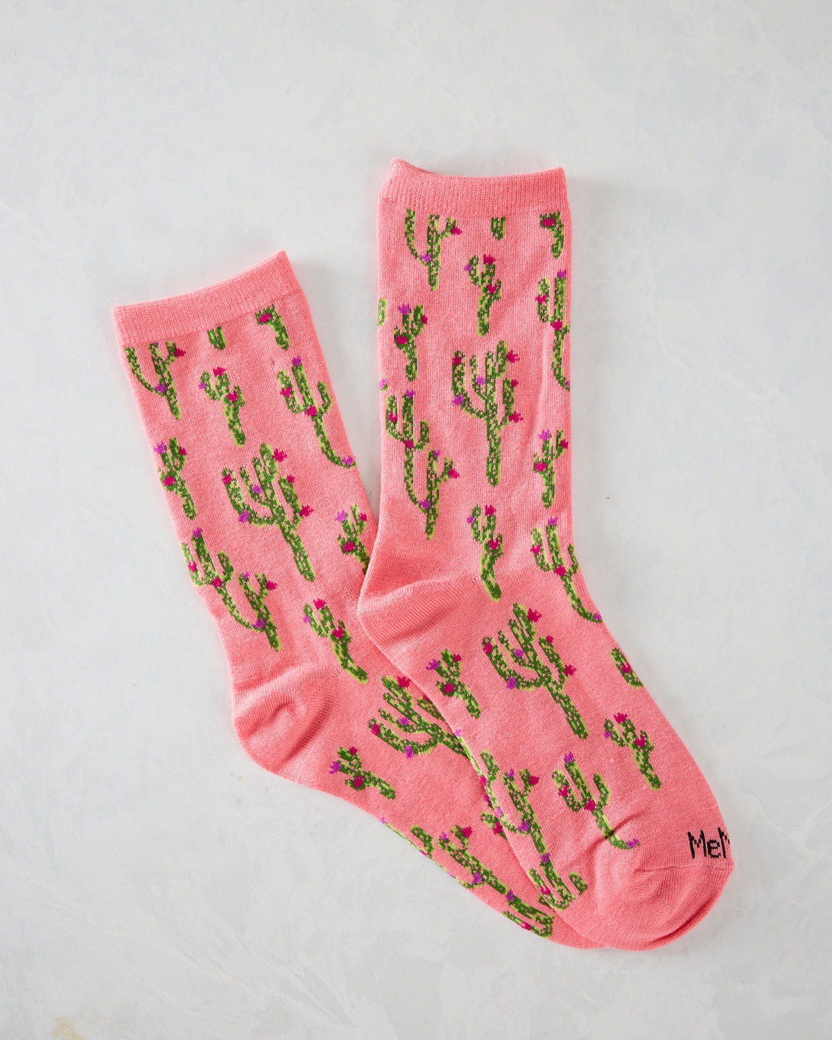 Pair of pink crew socks with repeating green cactus and pink and purple flower patterns.