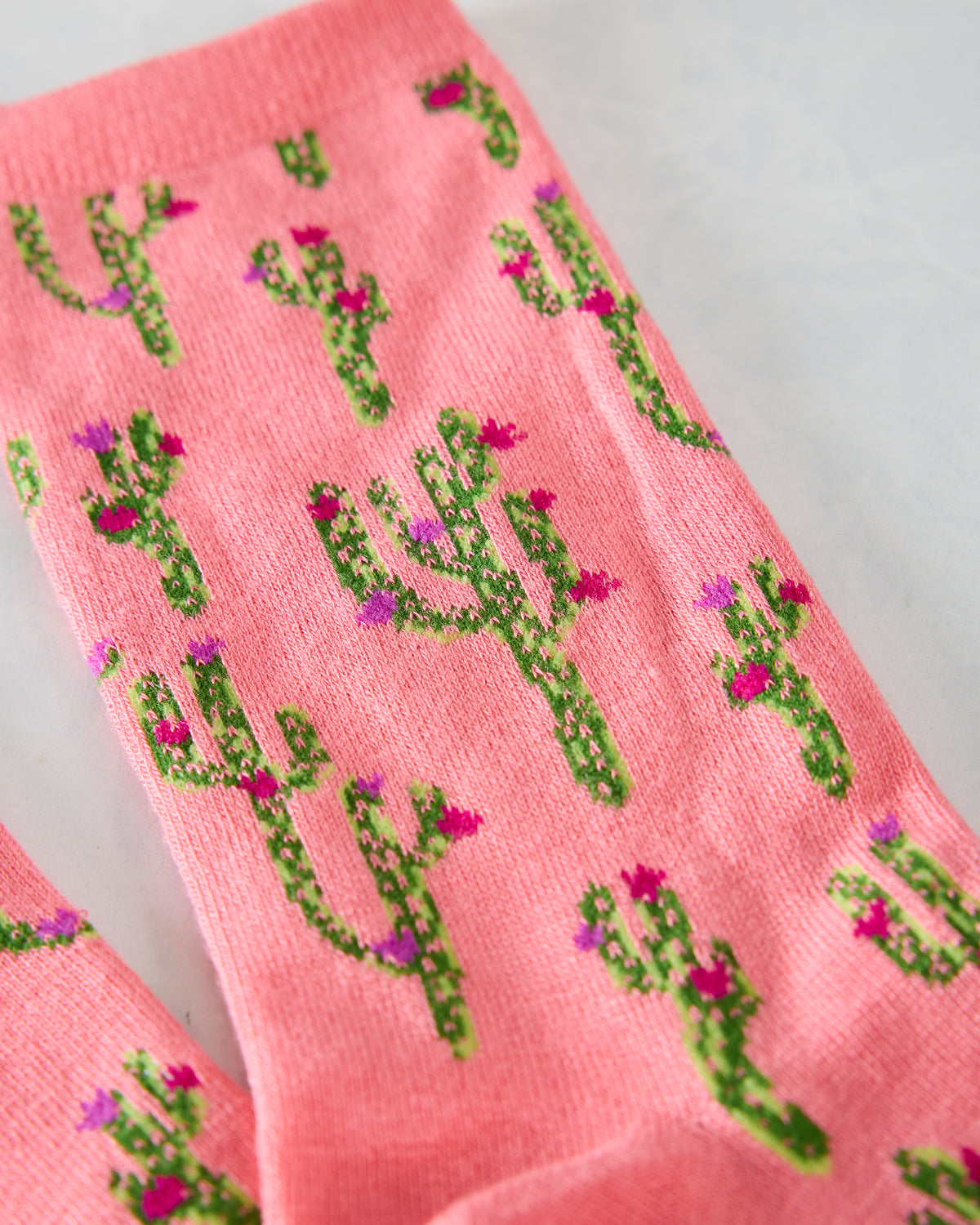 Close-up of the pink sock fabric with repeating green cactus and pink and purple flower patterns.
