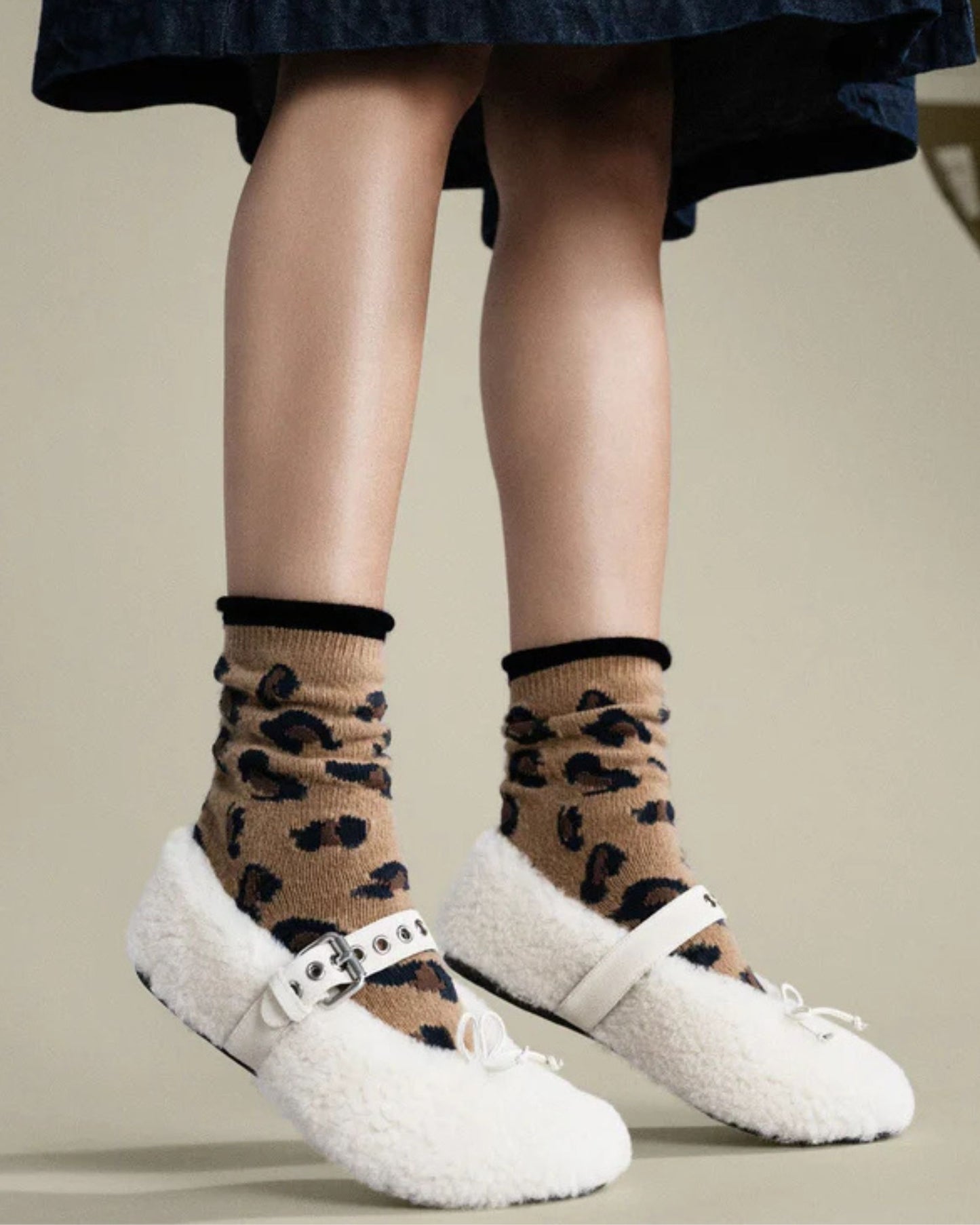 Person wearing camel animal-print crew socks with white Mary Jane-style shoes.
