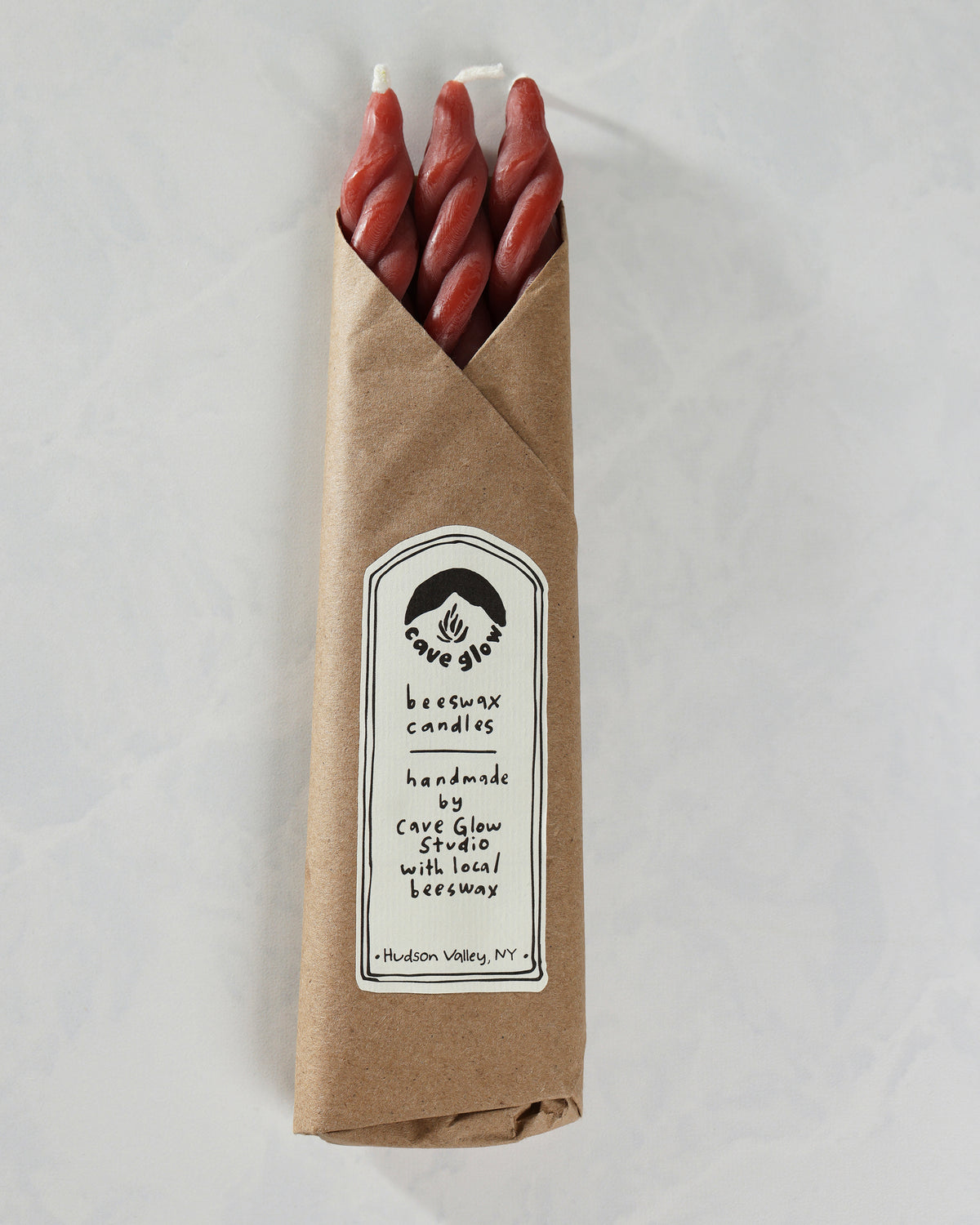 Packaged set of three red spiral candles in a brown paper sleeve with a Cave Glow Studio label.