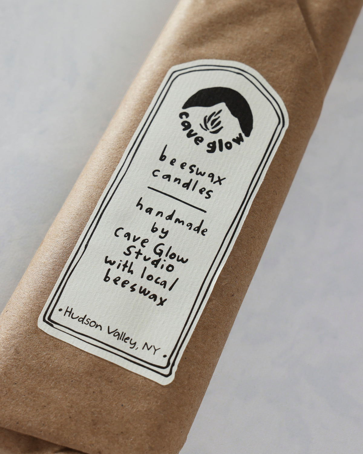 Close-up of the brown paper candle sleeve showing the Cave Glow Studio label for handmade beeswax candles.