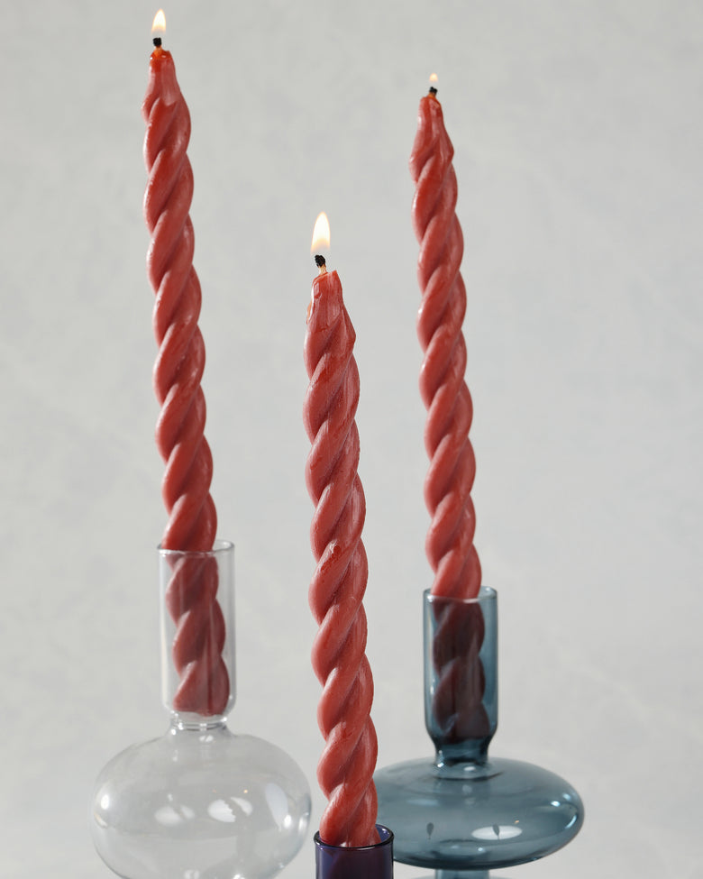 Three red spiral candles displayed in glass holders, with all three wicks lit.