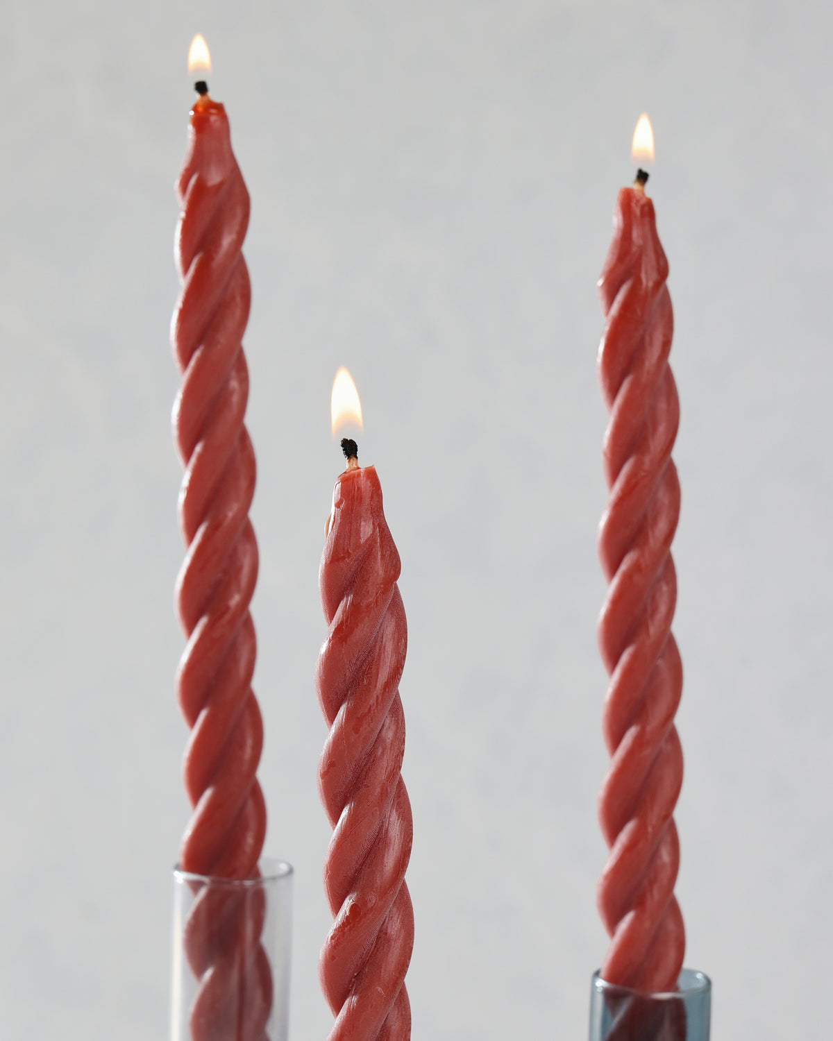 Close-up of three red spiral candles displayed in glass holders with lit wicks.