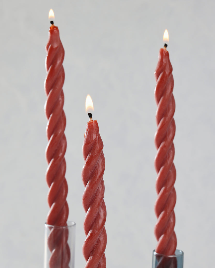 Close-up of three red spiral candles displayed in glass holders with lit wicks.