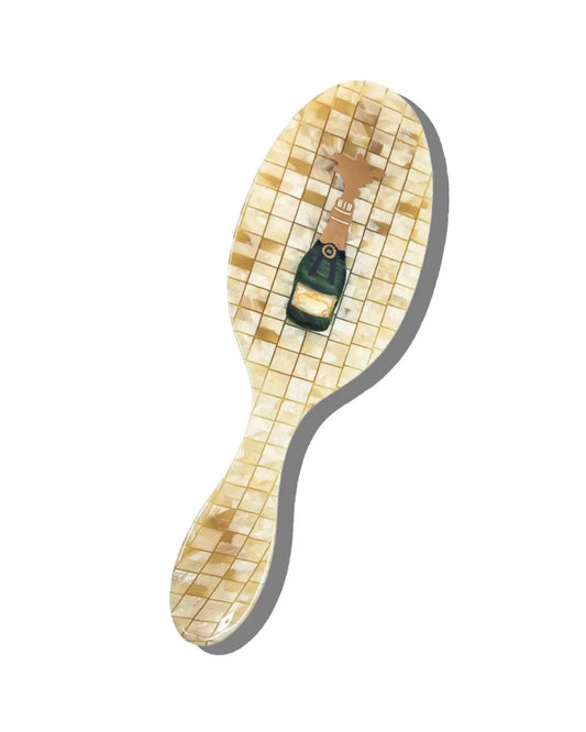 Hand-painted champagne-themed hair brush with a champagne bottle design and pale mosaic-patterned handle on a white background.