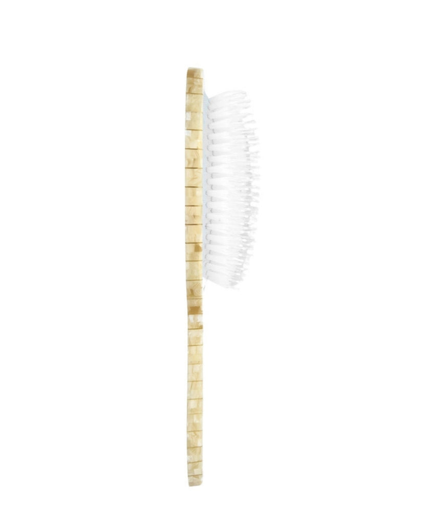 Side view of a champagne-colored hair brush showing its white bristles and slim profile.