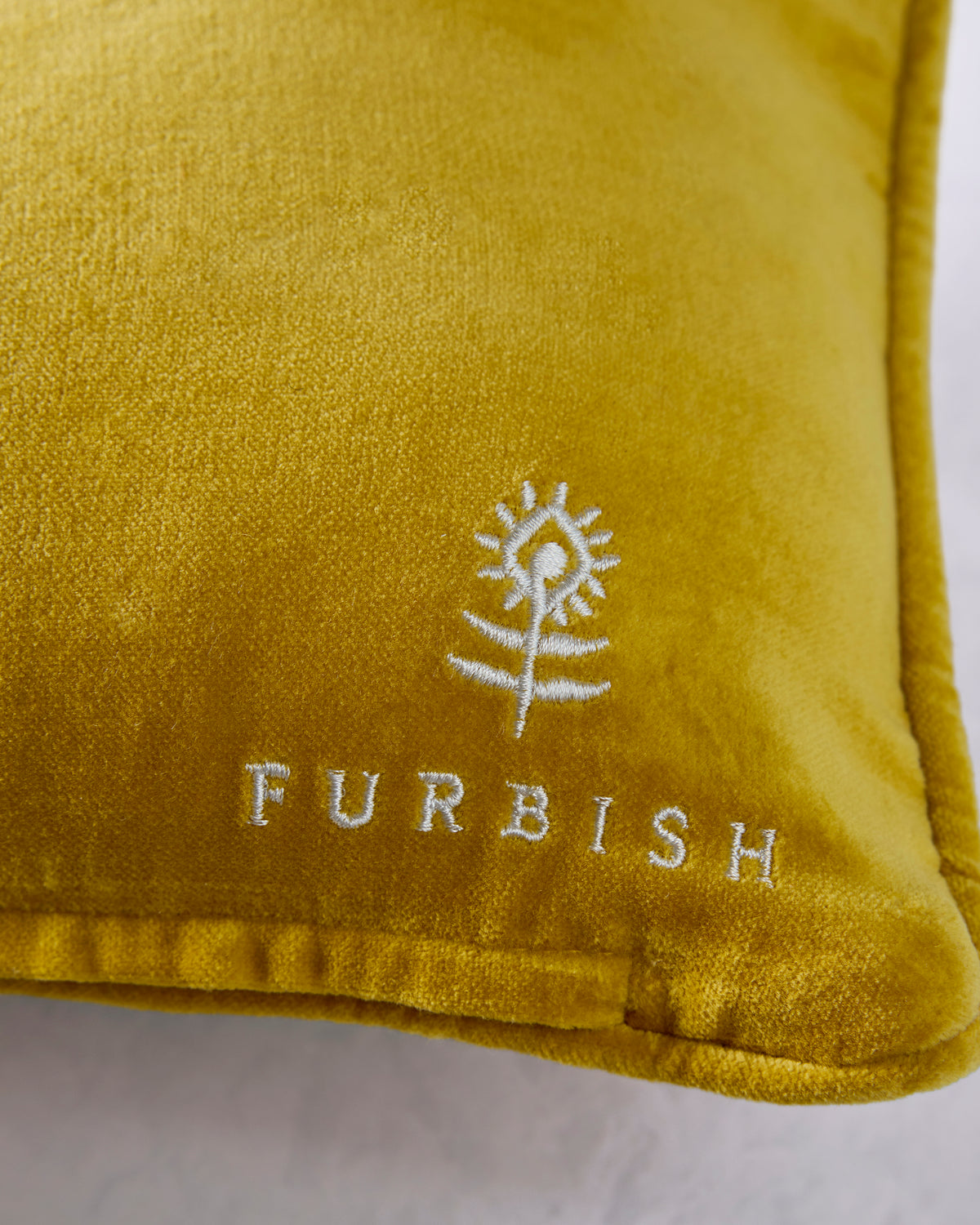 Close-up of the gold pillow showing the embroidered Furbish logo and the word “FURBISH.”