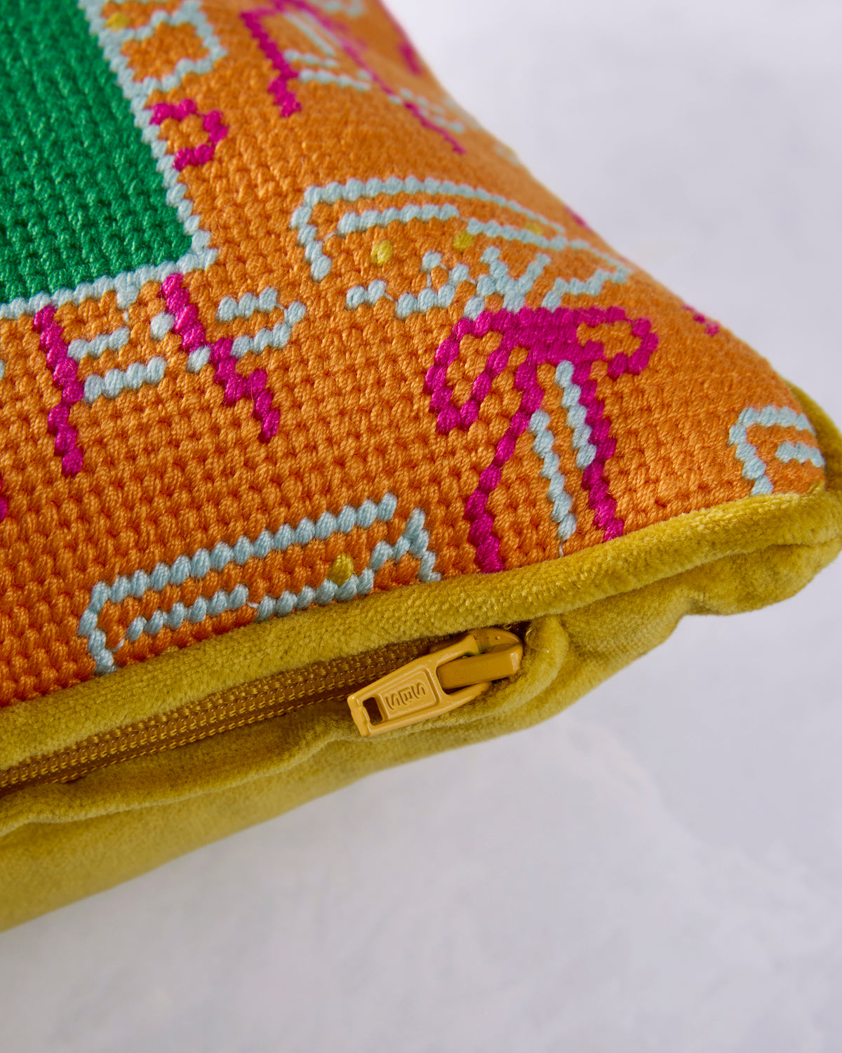 Close-up of the pillow’s colorful embroidered front, gold edging, and zipper closure.