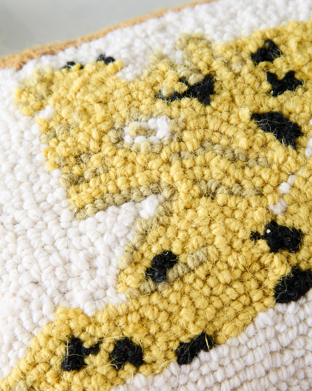 Close-up of the ivory hook pillow’s textured leopard motif in yellow, white, and black.