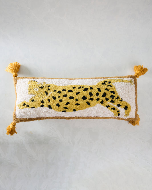 Ivory hook pillow with a spotted yellow leopard motif, brown edging, and four gold tassels.