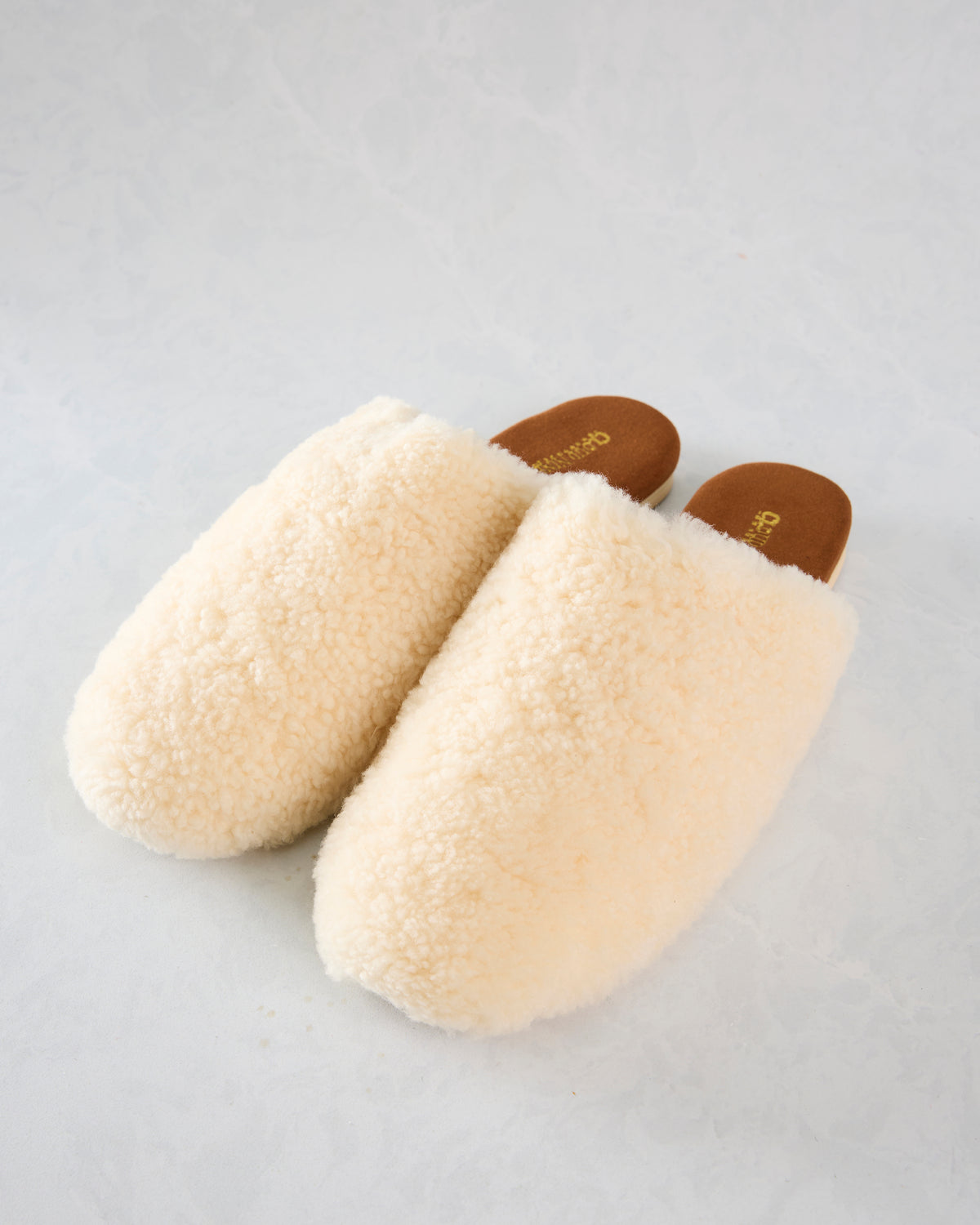 Pair of ivory Nora slide slippers with plush uppers and brown footbeds.
