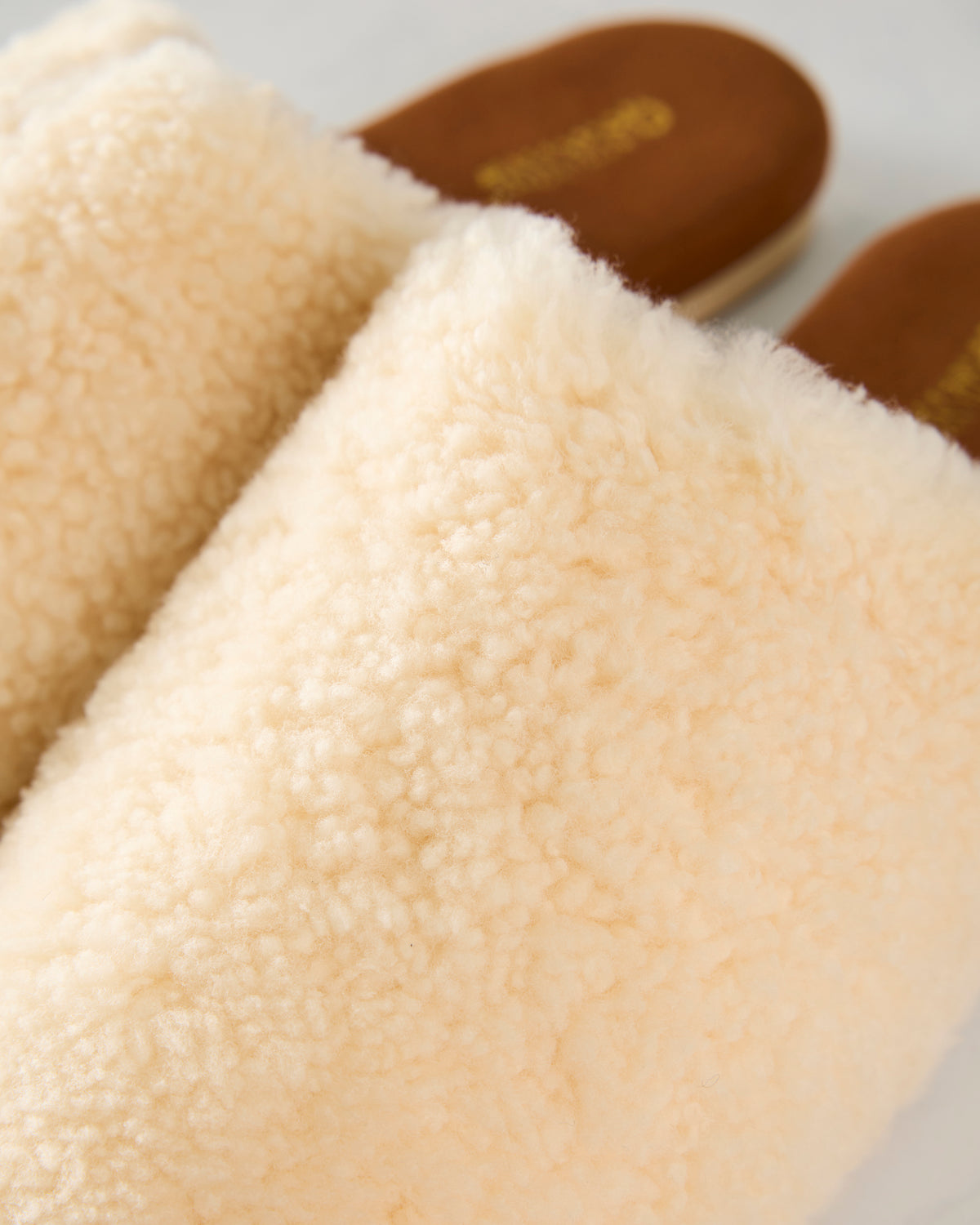 Close-up of the ivory plush upper and brown footbed of Nora slide slippers.