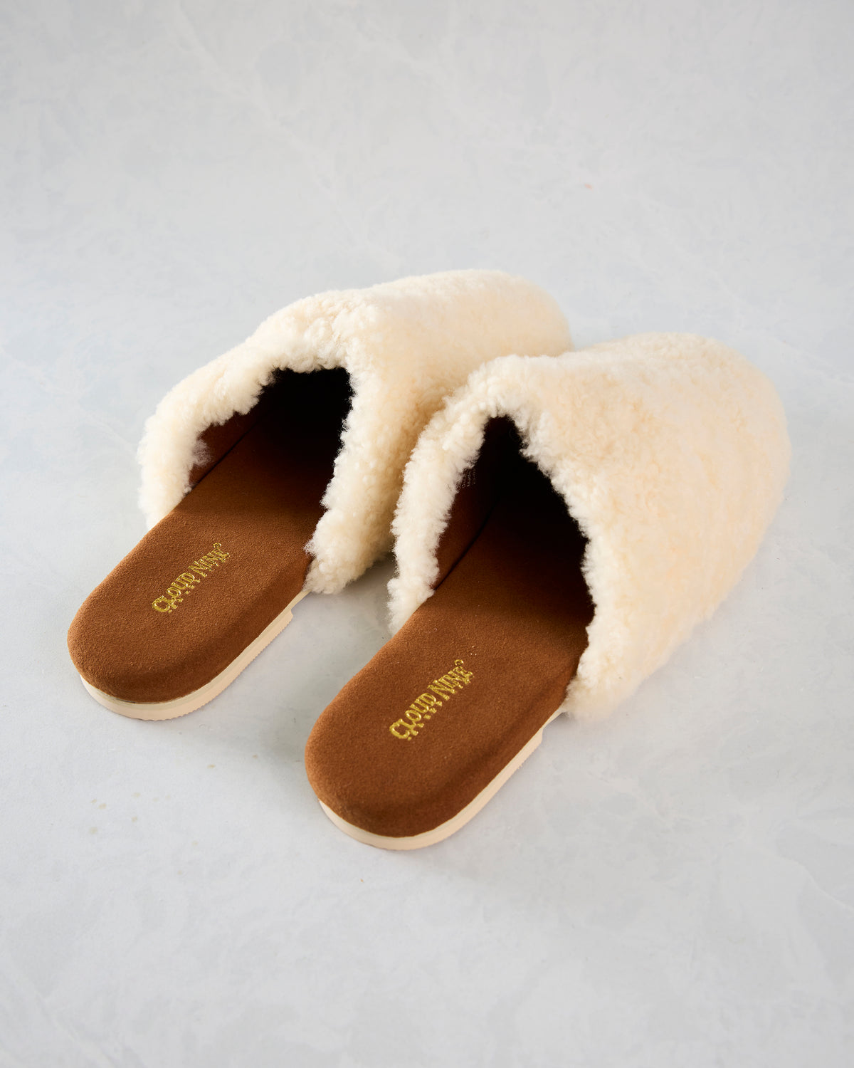 Pair of ivory Nora slide slippers with plush uppers and brown footbeds, shown from above.