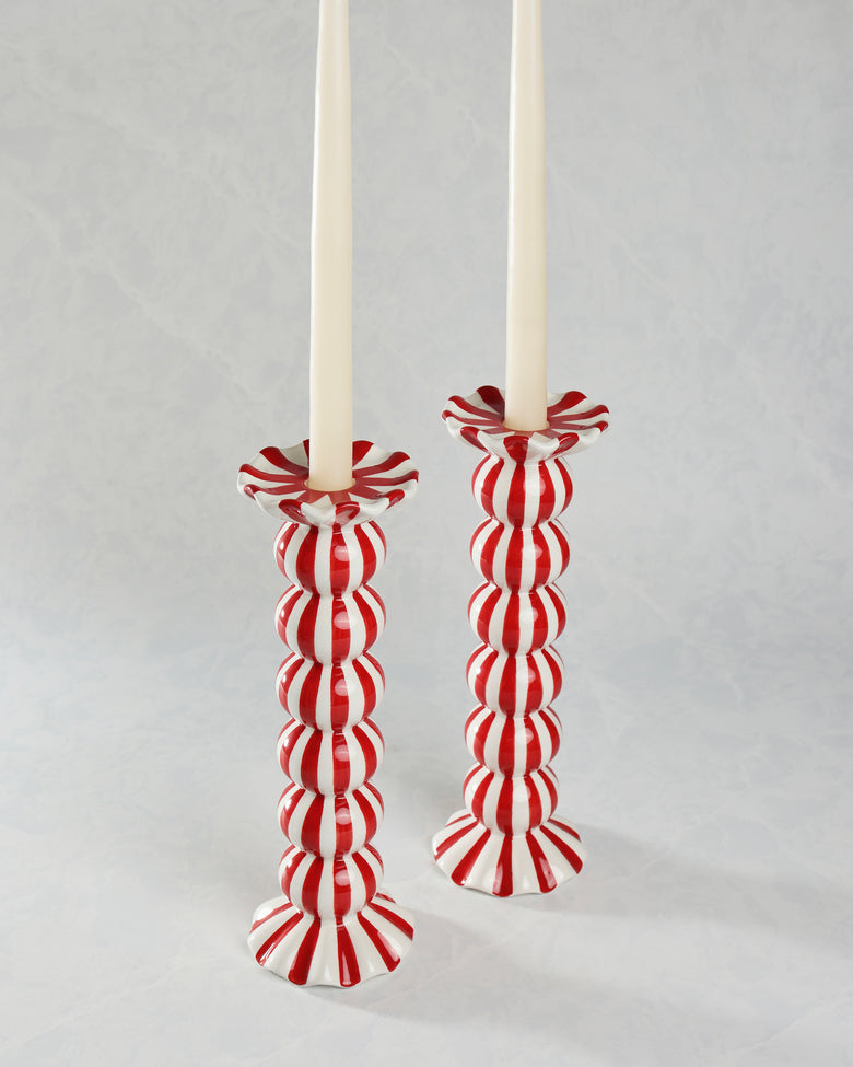 Two red-and-white striped ruffle candle holders holding tall white candles.