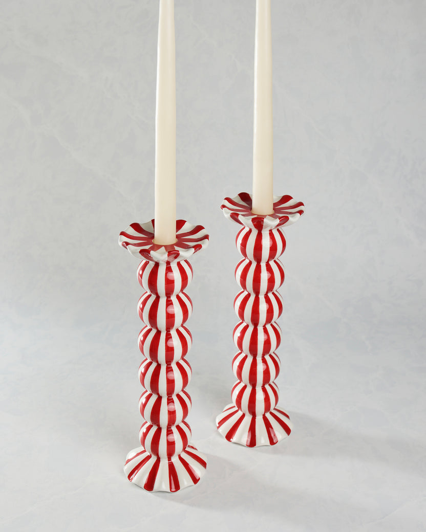 Two red-and-white striped ruffle candle holders holding tall white candles.