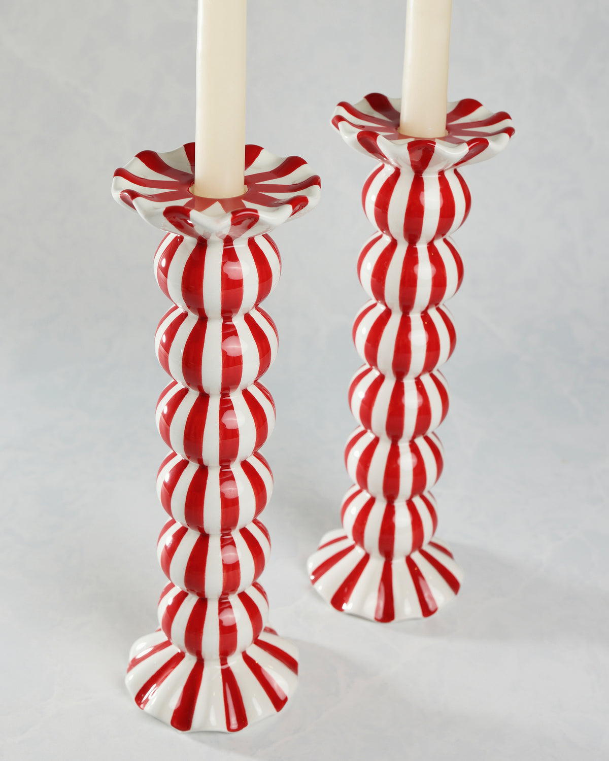 Close view of two red-and-white striped candle holders with ruffled candle cups and flared bases.