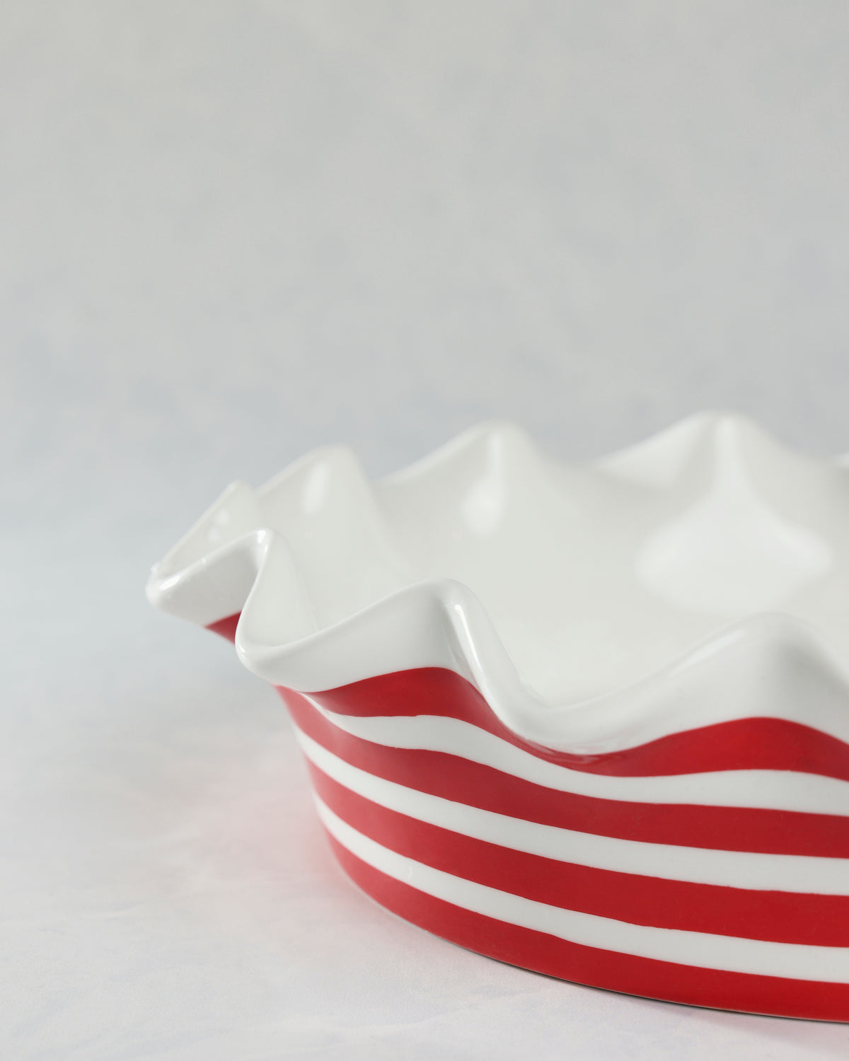 Close-up of a white ruffled pie dish with red horizontal stripes.