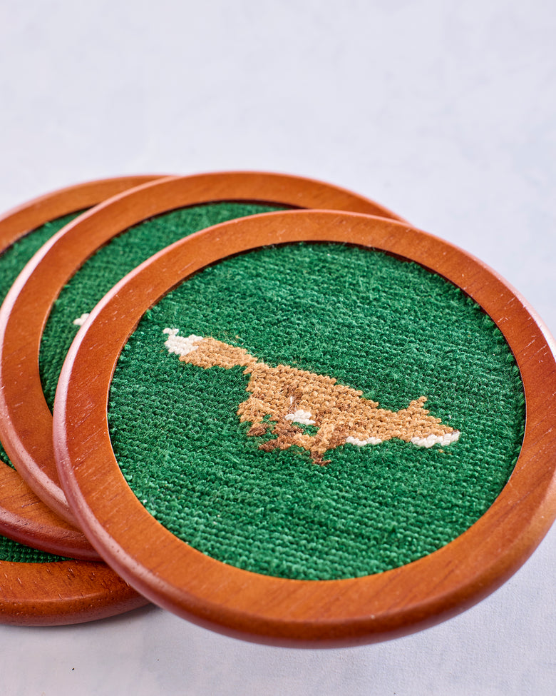 Close view of three overlapping wooden Fox Chase coasters with green needlepoint fox designs.